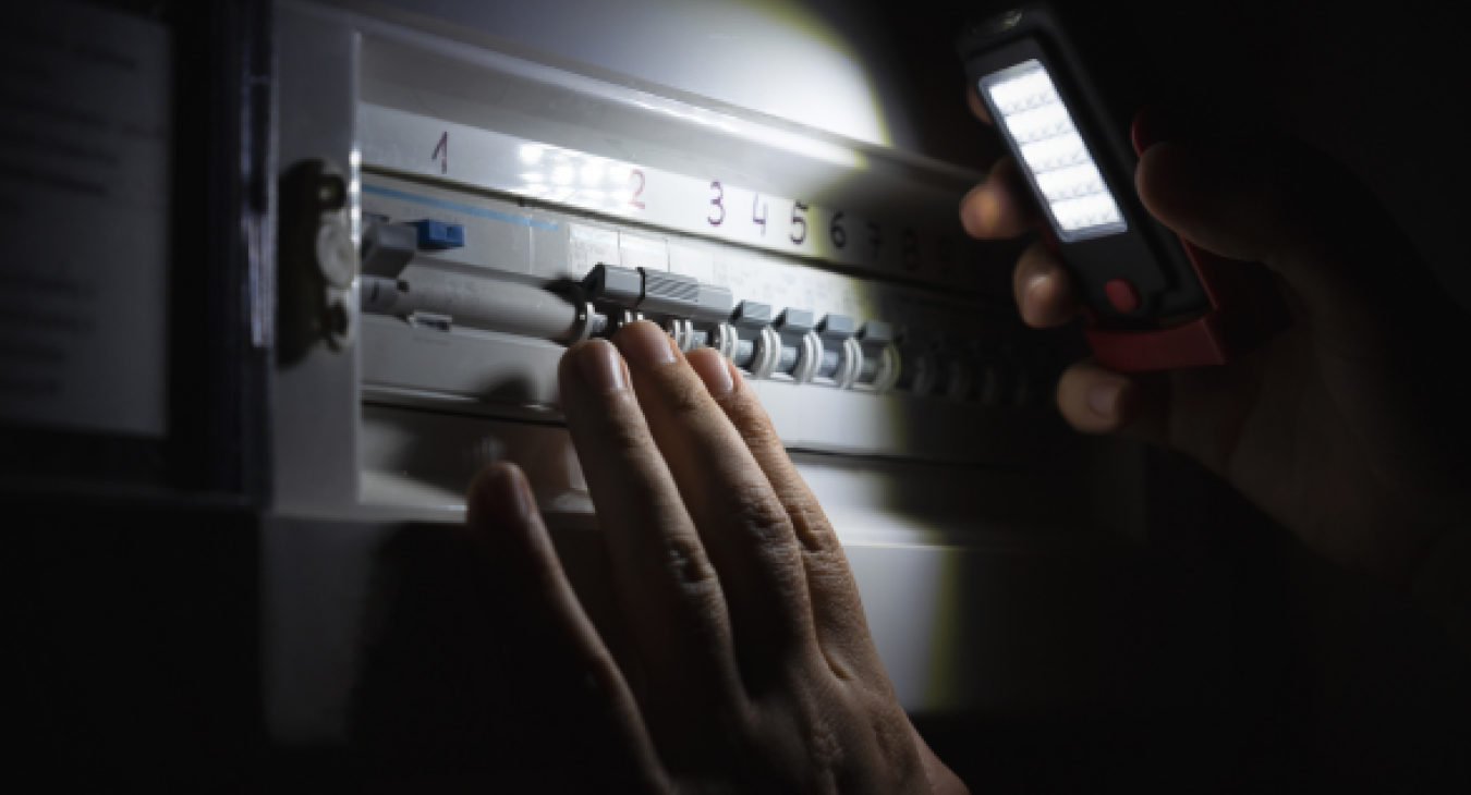 Person holding lit torch inspects consumer unit in darkened room - Electrical Faults Fixed